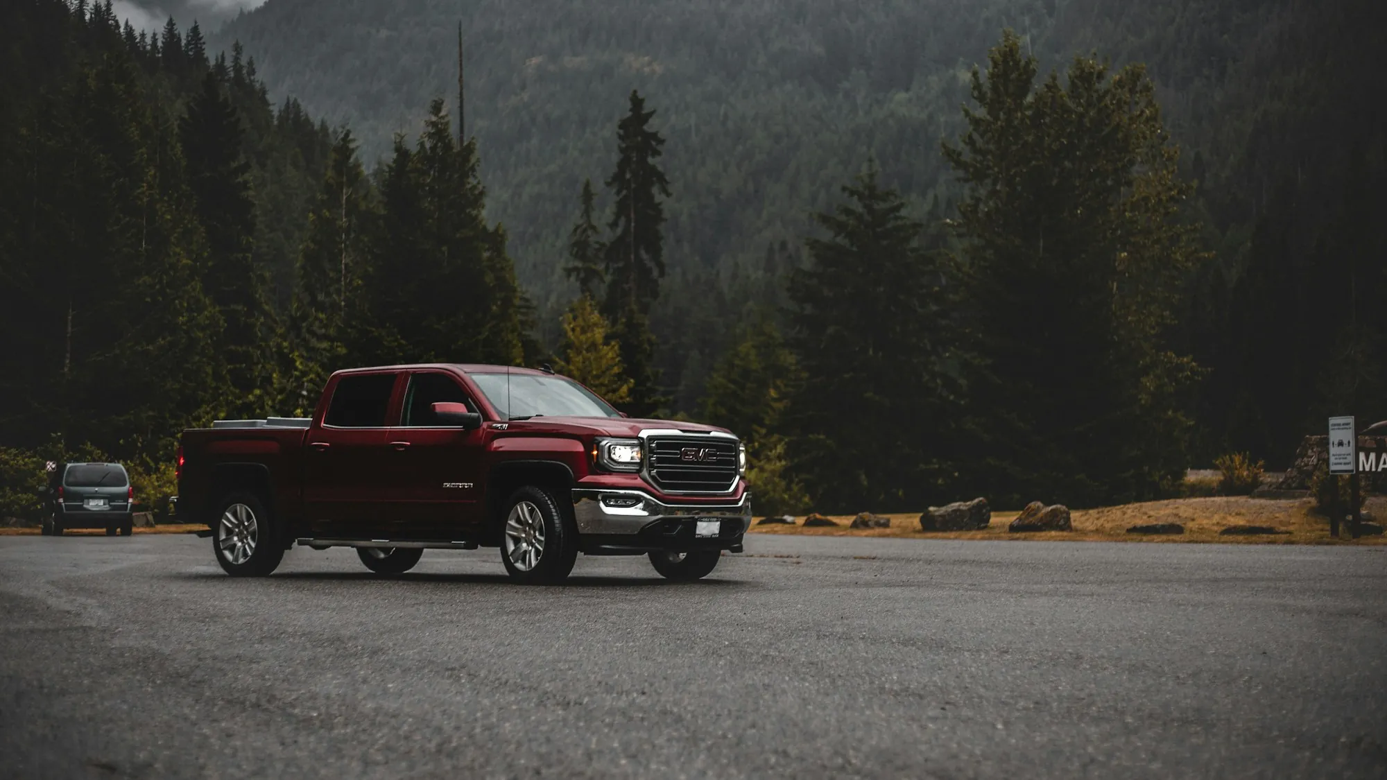 Red pickup truck parked beside a forest