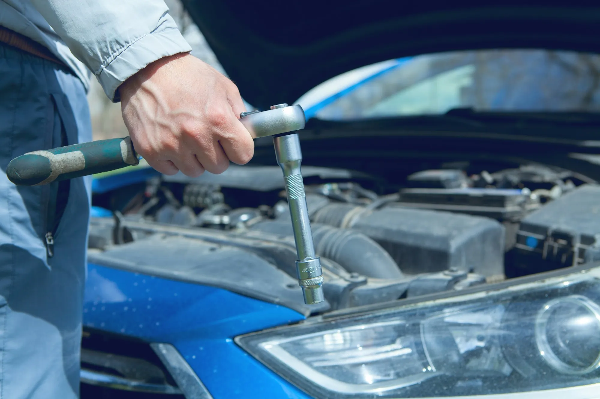 Hand turning a ratchet on an engine under an open hood
