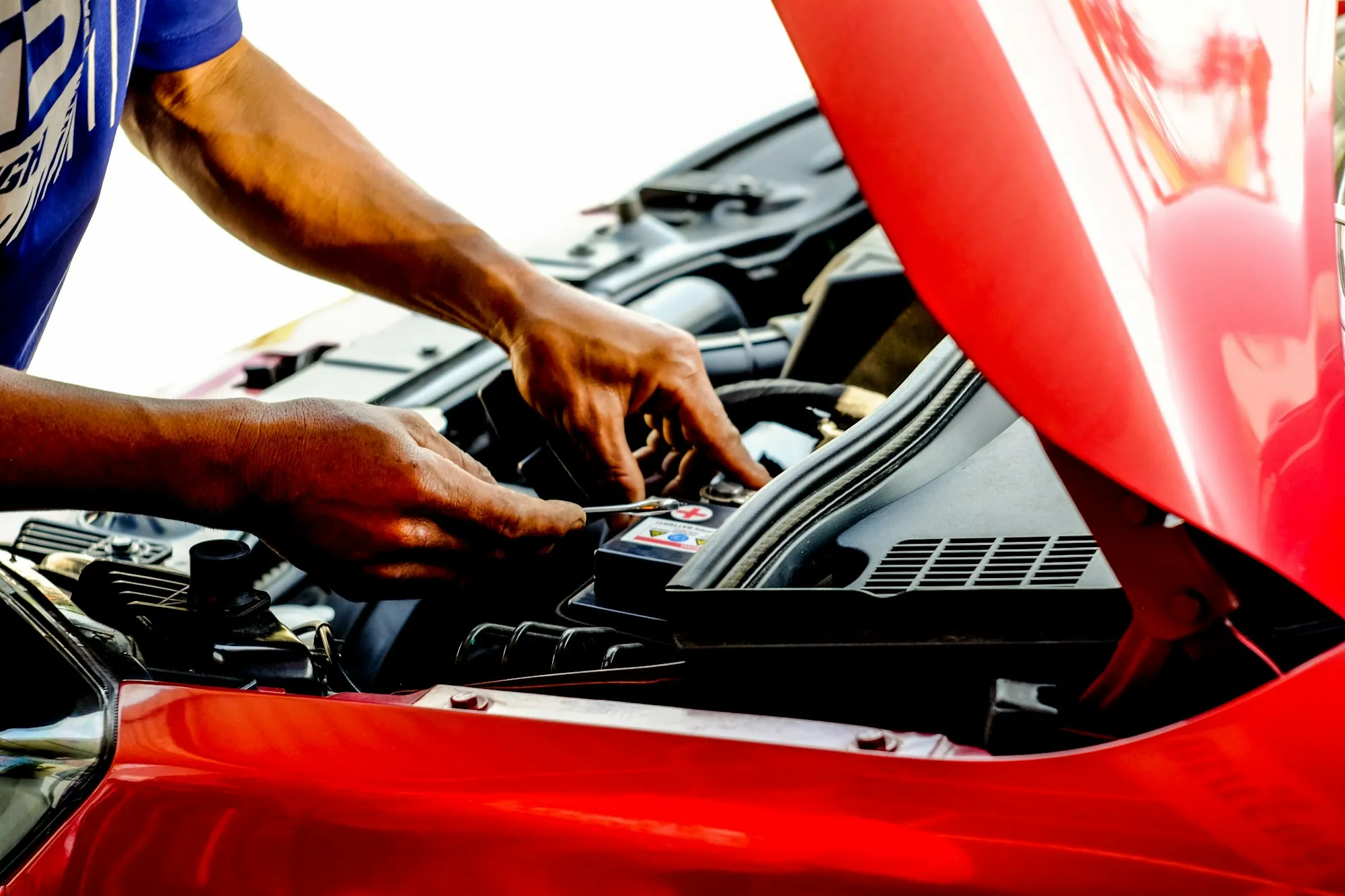 Mechanic's hands working in the engine bay of a red car