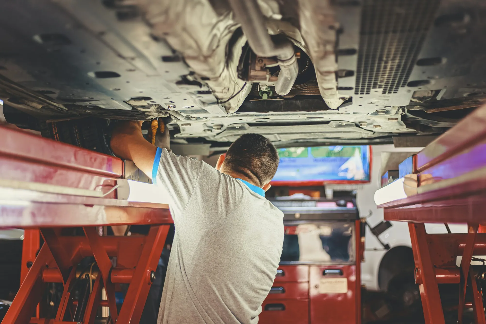 Mechanic working beneath a car raised on red lift arms
