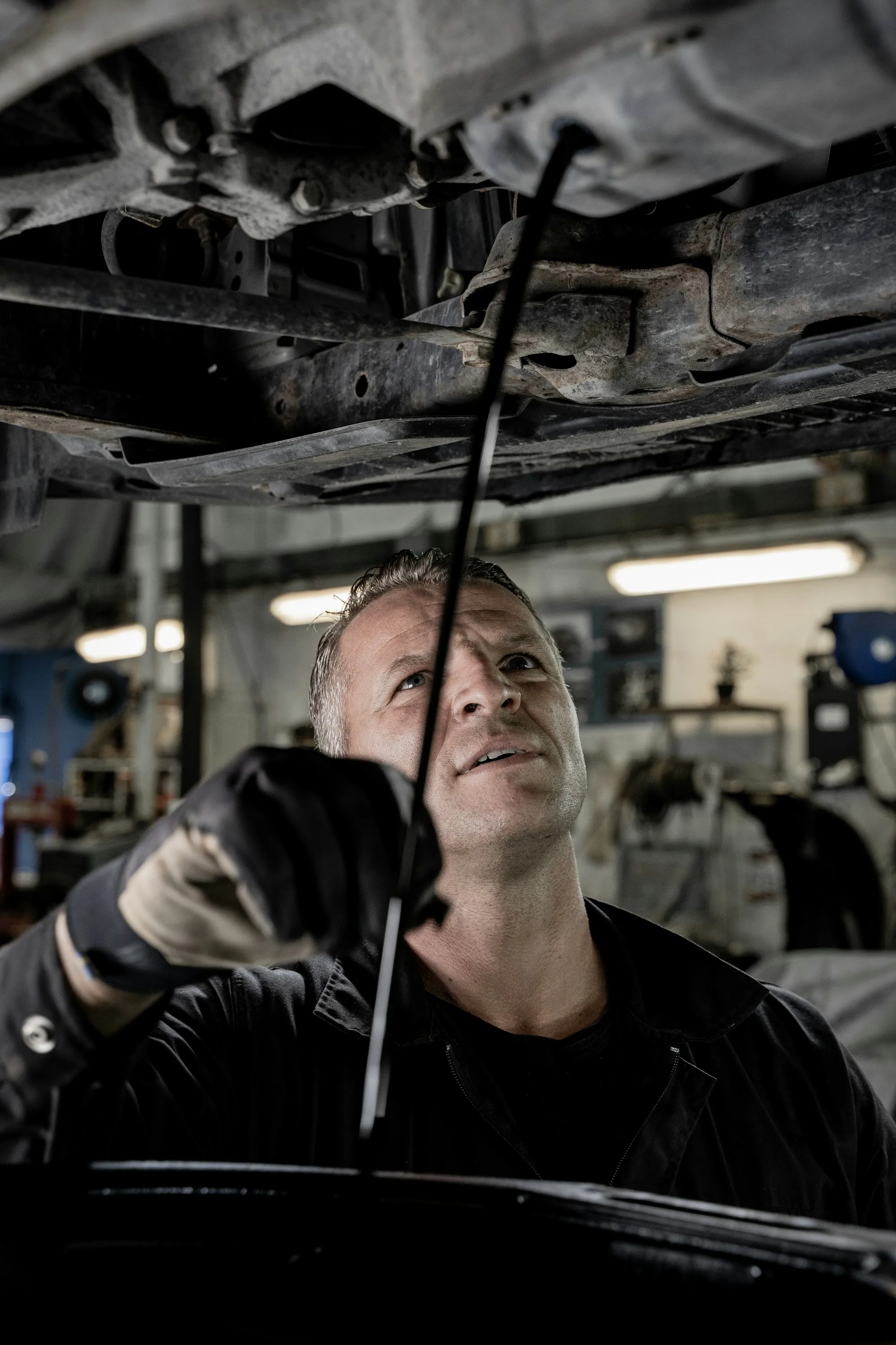 Mechanic in a dark jacket reaching up under a raised car