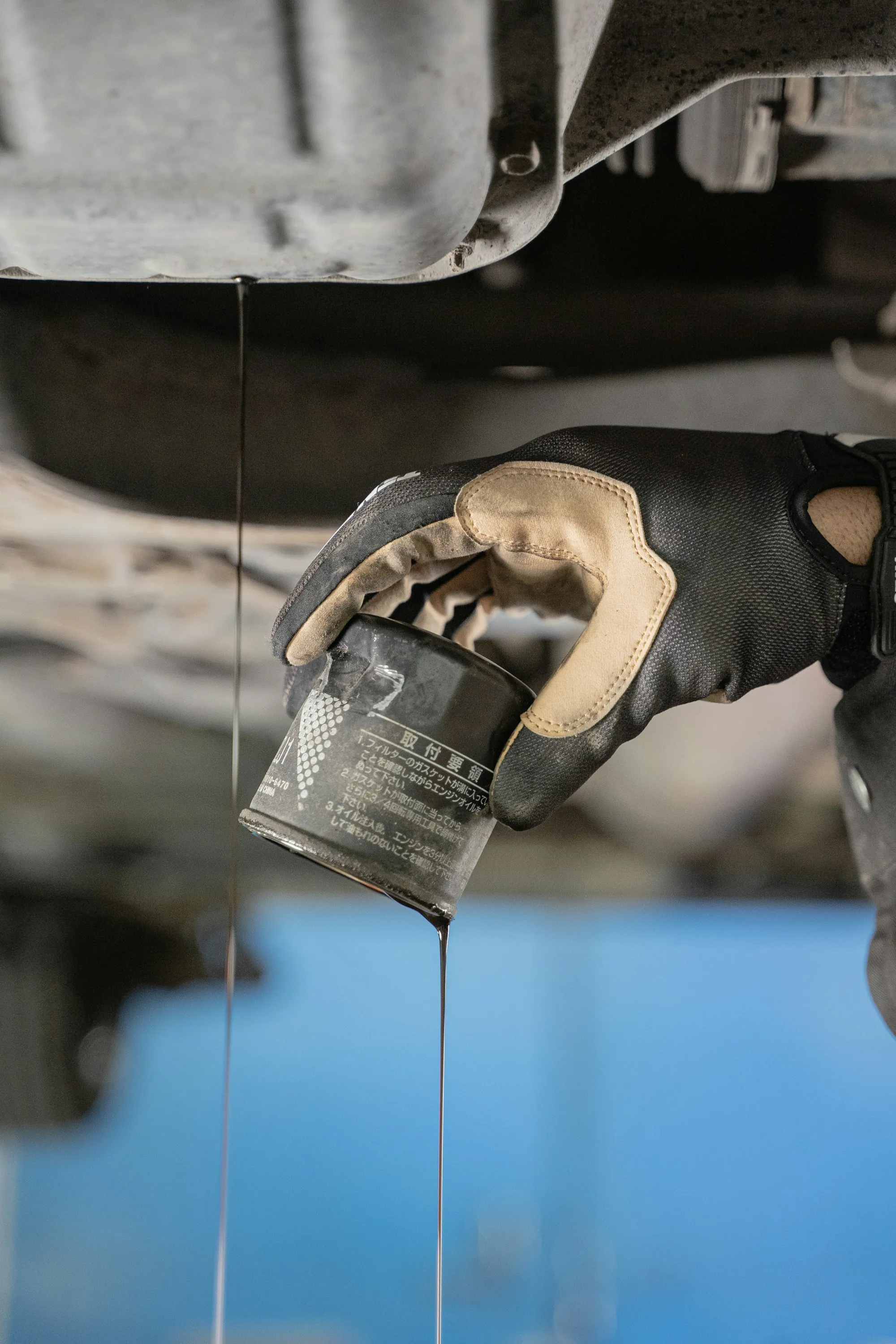 Gloved hand holding an oil filter under a car